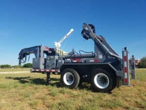 A crane truck parked in the grass near some trees.