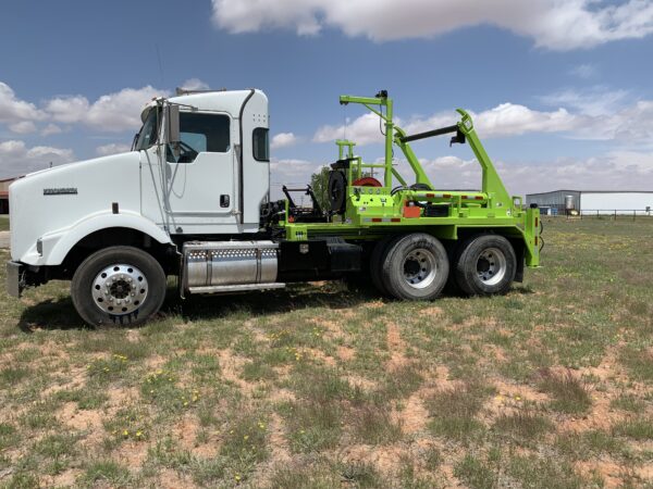 A white truck with green tow truck in the middle of a field.