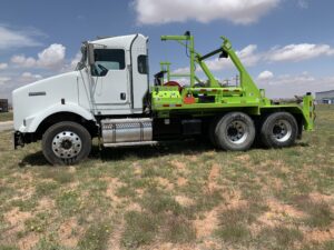 A white and green tow truck parked in the grass.