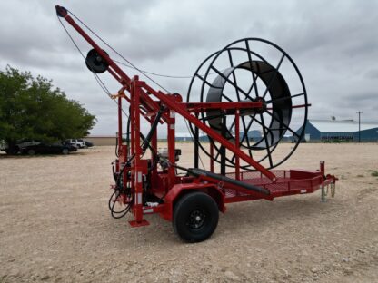 Red cable spool trailer on gravel lot.